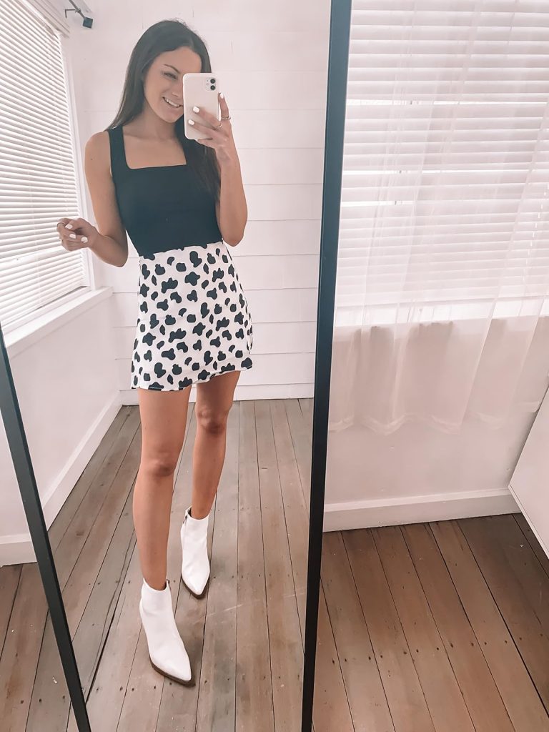 Nashville outfits from Amazon: black tank top, white ankle boots, and a satin cow-print skirt